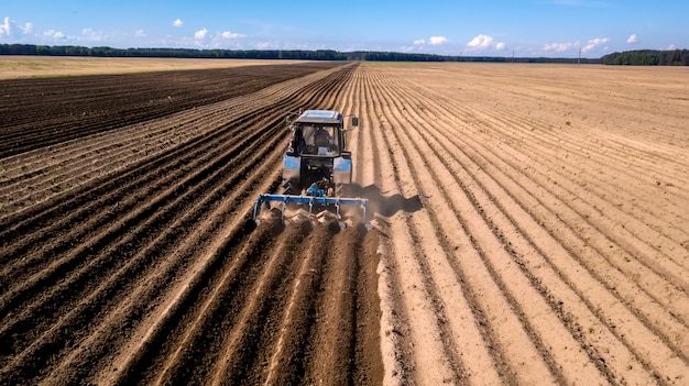 Tractor - aerial view of a tractor at work - cultivating a field in spring with blue sky - agricultural machinery