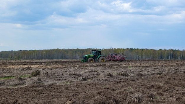 Tractor cultivates the land in a field located near the forest