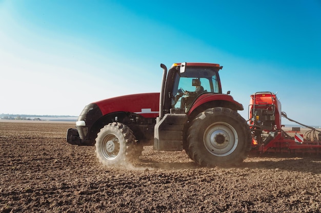 The tractor performs field work. Modern red tractor in the agricultural field. Tractor plowing land.