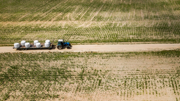 Tractor rides on the field and carries bales of hay aerial view