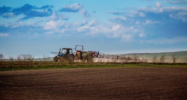 A tractor with a fertilizer sprayer trailer preparing the land for crops and a beautiful sky in spring