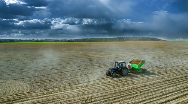 Tractors at work in a field cultivating the soil ready for potatoes to be planted. Aerial view.