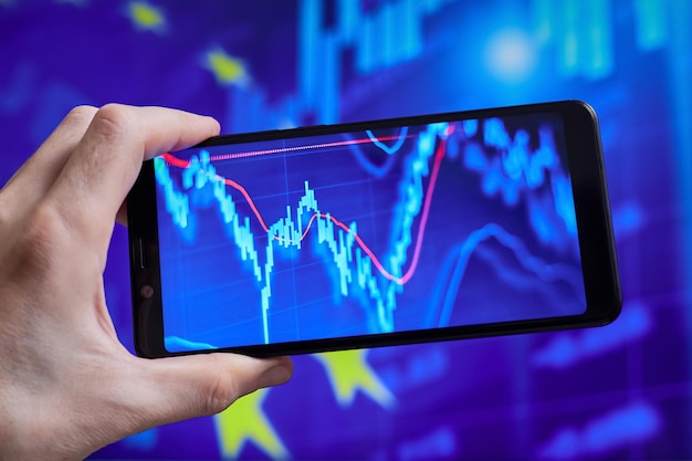 Trader analyzes stock market data in smartphone on the background of stock charts