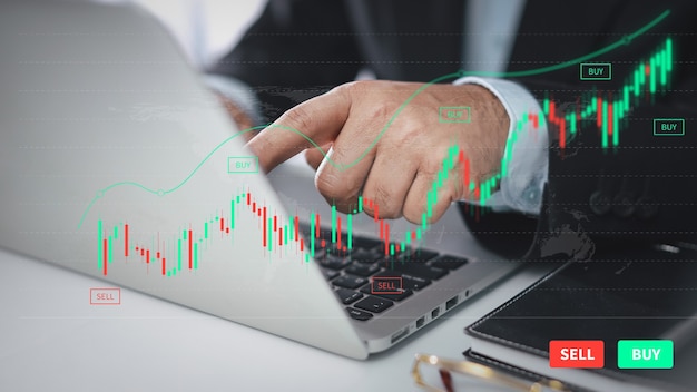 Trader or businessman hands showing virtual hologram price graph and indicator, red and green candlestick chart stock trading on laptop computer and smartphone. Investing on stock concept.