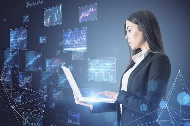 Trading investing and data flow concept with businesswoman using laptop on digital wall background with stock market graphs and indicators on many screens background Double exposure