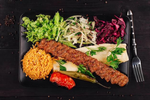 Traditional adana kebab serving with bulgur salad and lavash bread on black plate