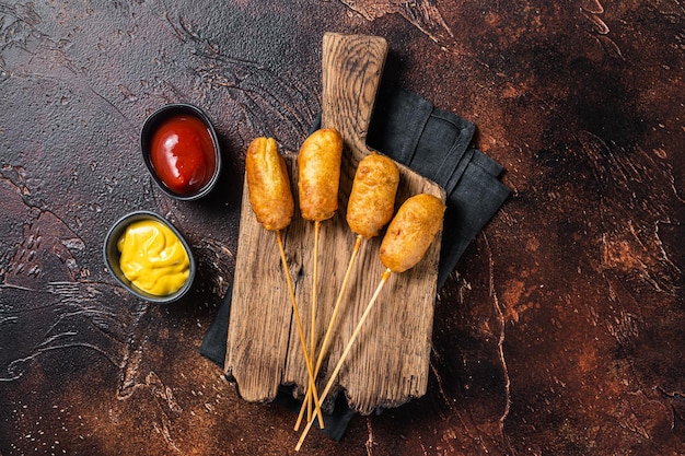 Traditional American street junk food Deep fried corn dogs with mustard and ketchup Dark background Top view