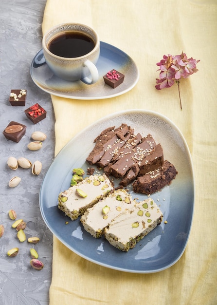 Traditional arabic sweets sesame halva with chocolate and pistachio and a cup of coffee on a gray concrete background side view close up