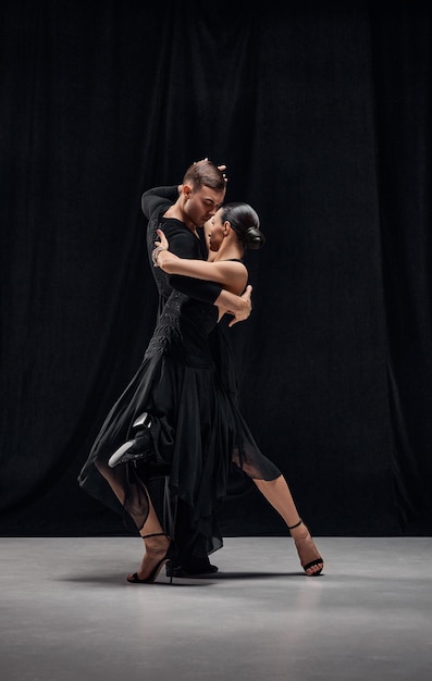 Traditional choreography Man and woman professional tango dancers performing in black stage costumes over black background