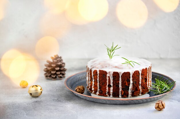 Traditional Christmas cake with fruits and nuts on a light table and light background. Dessert for the winter holidays. Christmas decorations and lights. Copy space