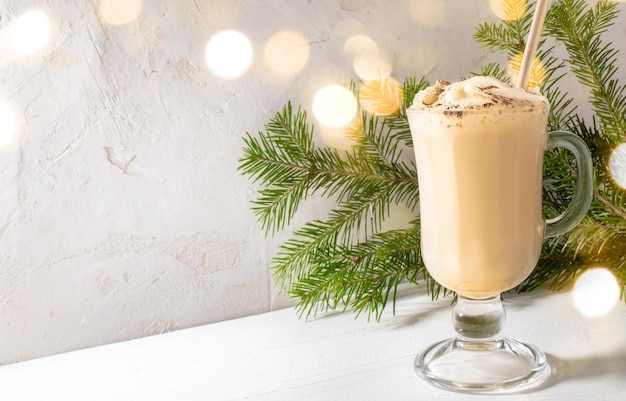 Traditional Christmas drink Eggnog in glass fir branches with Christmas lights on white backdrop