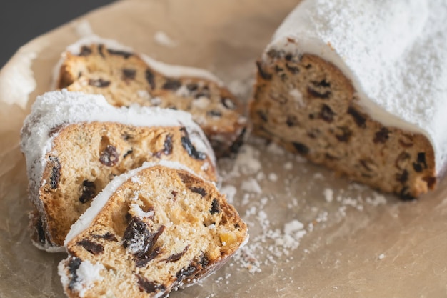 Traditional Christmas stollen made of dried fruits and nuts sprinkled with powdered sugar on the background of a Christmas decor with candles. Traditional Christmas cupcake.