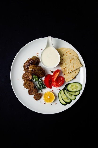 Traditional Cypriot Seftalia dish grilled with vegetables pita and sauce  on a black background