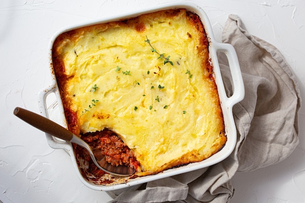 Traditional dish of British cuisine Shepherd's pie casserole with minced meat and mashed potatoes in ceramic baking dish on white rustic table with spoon from above