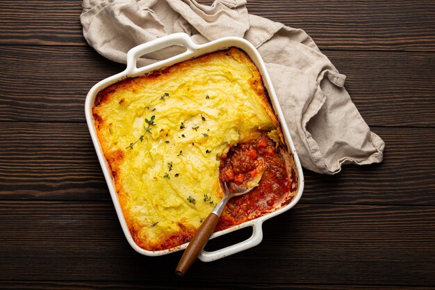 Traditional dish of British cuisine Shepherd's pie casserole with minced meat and mashed potatoes in ceramic baking dish on white rustic table with spoon from above