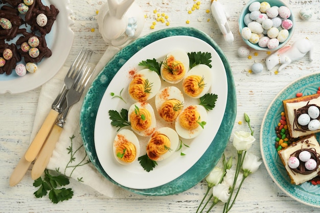 Traditional Easter brunch or dinner with stuffed eggs with paprika carrot cake bars and chocolate nest cakes with glazed walnut eggs Easter meal dishes with holday decorations Top view flat lay