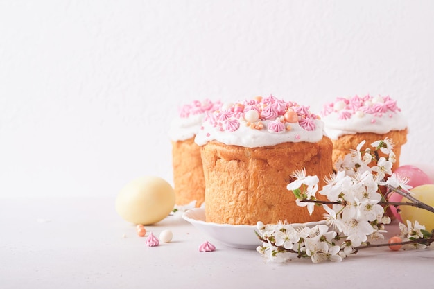 Traditional Easter sweet bread or cakes with white icing and sugar decor colored eggs and cherry blossom tree branch over white table Various Spring Easter cakes Happy Easter day Selective focus