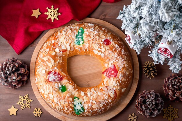 Traditional Epiphany cake Roscon de Reyes on wooden table top with small Christmas tree and decoration closeup, top view