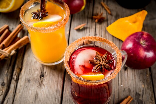 Traditional fall and winter drinks and cocktails. White and red autumn hot spicy sangria with anise, cinnamon, apple, orange, wine. In glass mugs, old rustic wooden table. Selective focus copy space