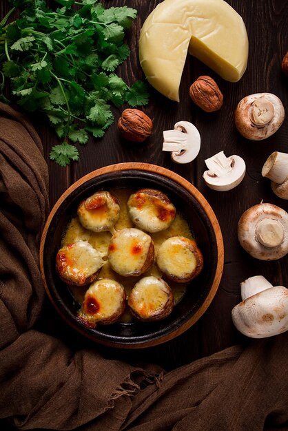 Traditional Georgian dish appetizer stuffed mushrooms Sulguni cheese baked in a Ketzi clay pan on a wooden table closeup no people