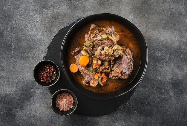 Traditional German braised beef cheeks in brown red wine sauce with herbs as closeup in black plate