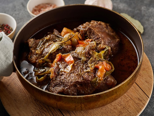 Traditional German braised beef cheeks in brown red wine sauce with herbs as closeup in skillet