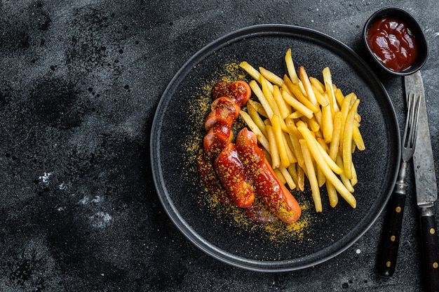 Traditional German currywurst, served with French fries. Black table. Top view. Copy space.