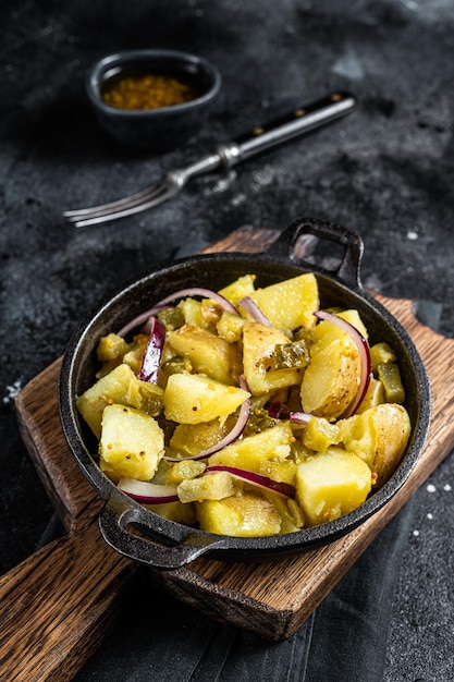 Traditional German Kartoffelsalat potato salad with cucumber onion and mayonnaise in a skillet Black background Top view