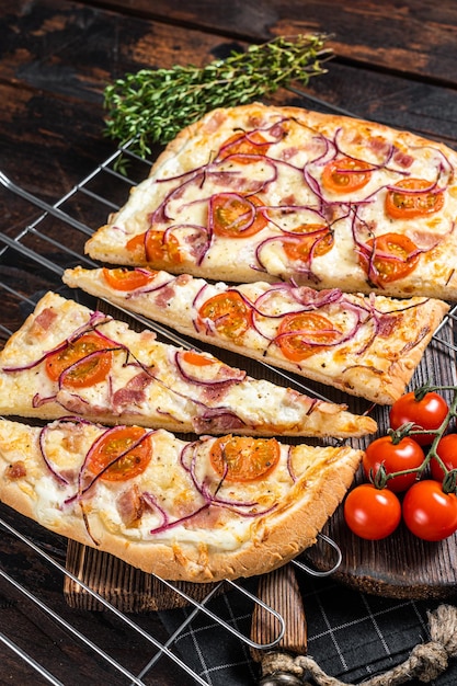 Traditional German pie Flammkuchen or tarte flambee with cream cheese bacon tomato and onions Wooden background Top view