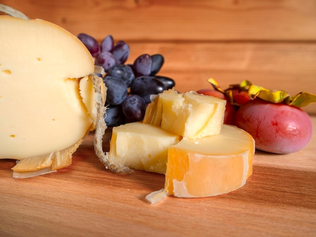 Traditional Greek smoked cheese Metsovone on a wooden board with grapes and persimmons in Greece