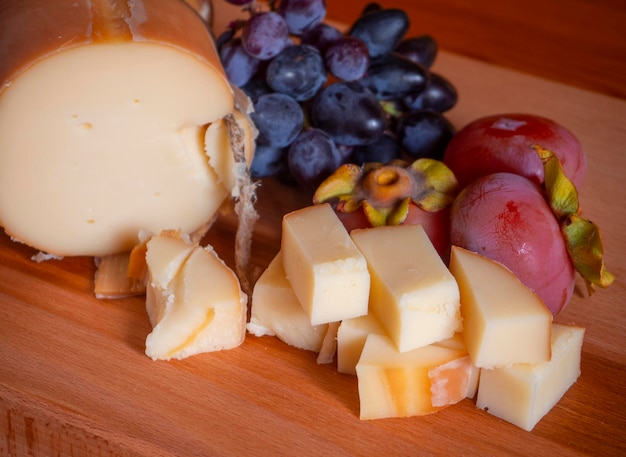 Traditional Greek smoked cheese Metsovone on a wooden board with grapes and persimmons in Greece