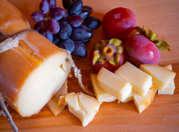 Traditional Greek smoked cheese Metsovone on a wooden board with grapes and persimmons in Greece