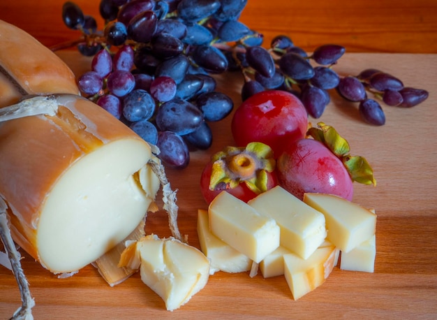 Traditional Greek smoked cheese Metsovone on a wooden board with grapes and persimmons in Greece