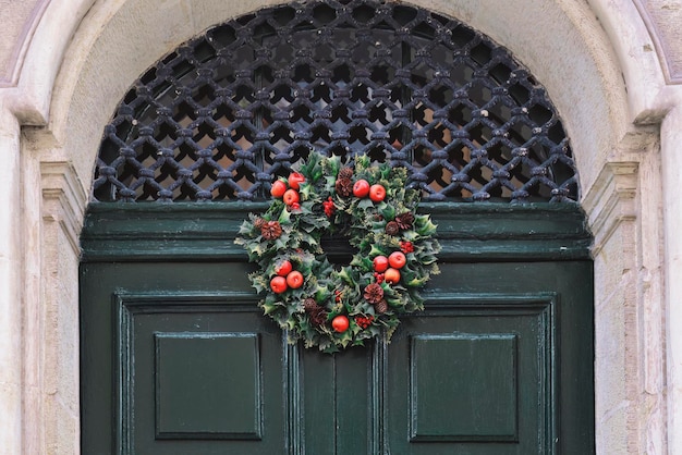 Traditional green and red Christmas wreath hanging on entrance door of house