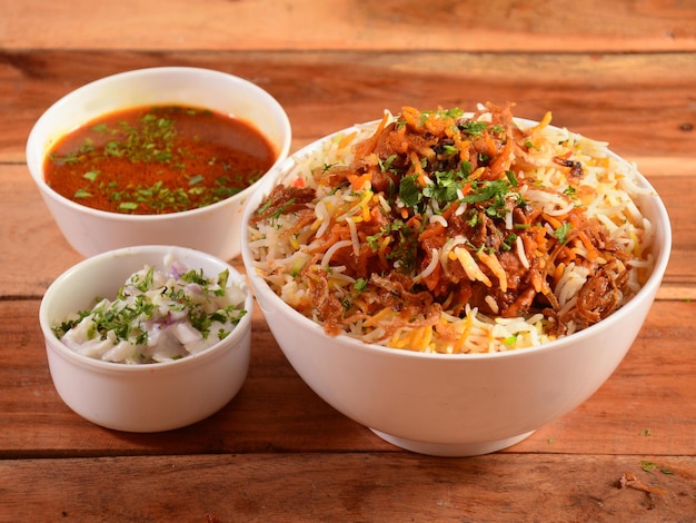 Traditional Hyderabadi Chicken dum Biryani made of Basmati rice cooked with masala spices served with Onion raita and Salan selective focus