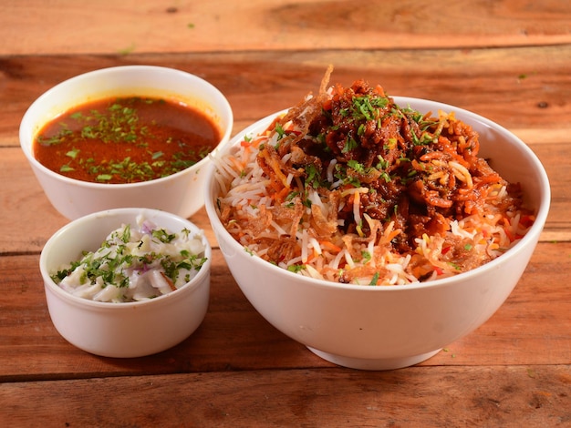 Traditional Hyderabadi Chicken dum Biryani made of Basmati rice cooked with masala spices served with Onion raita and Salan selective focus