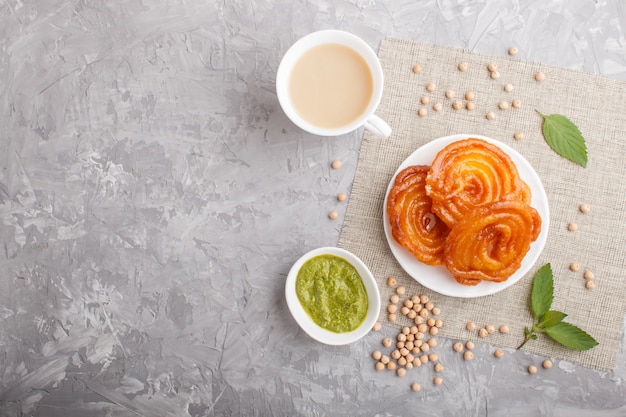 Traditional indian candy jalebi in white plate with mint chutney on a gray concrete copyspace. top view.