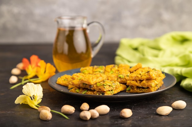 Traditional iranian dessert sohan with glass of green tea on a black concrete background side view close up