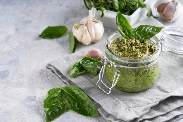 Traditional italian basil pesto sauce in a glass jar on a light stone table 