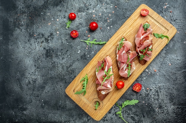 Traditional Italian bruschetta with dried tomatoes, prosciutto and arugula on a wooden board. banner, menu, recipe place for text, top view.