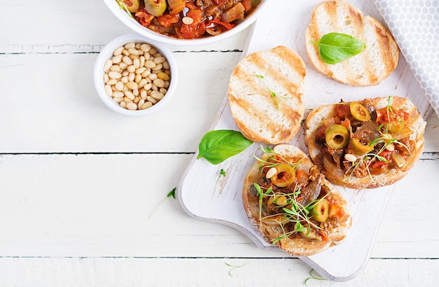 Traditional Italian Caponata and toast on a wooden white table. Sicilian caponata