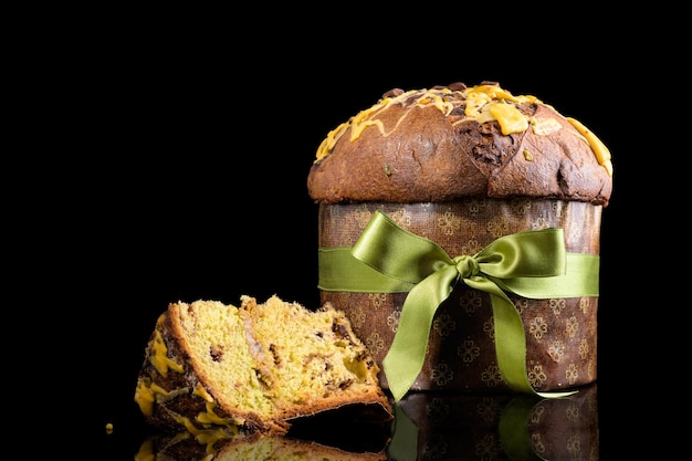 Traditional italian christmas cake panettone with green bow with cut piece of cake isolated on black