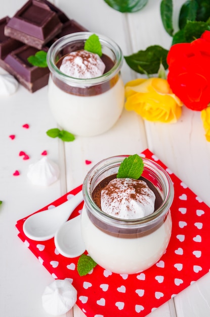 Traditional Italian dessert panna cotta with chocolate sauce and crispy meringue, dessert for Valentine's Day served in glass jars.