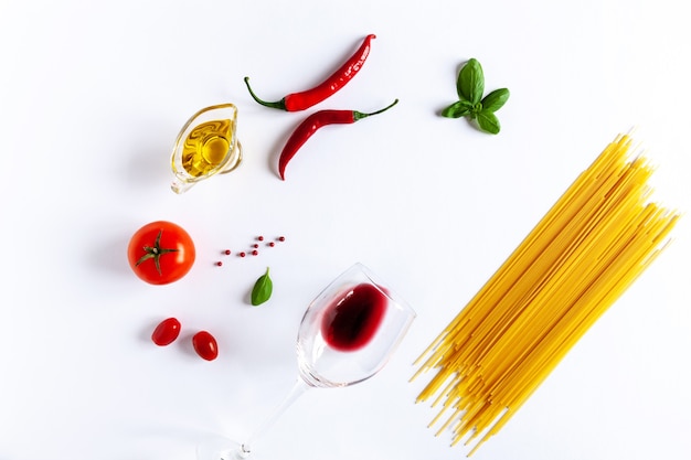 Traditional Italian pasta spaghetti,  tomatoes, basil, olive oil, chili pepper and glass of red wine . Top view, close-up, copy space on white background