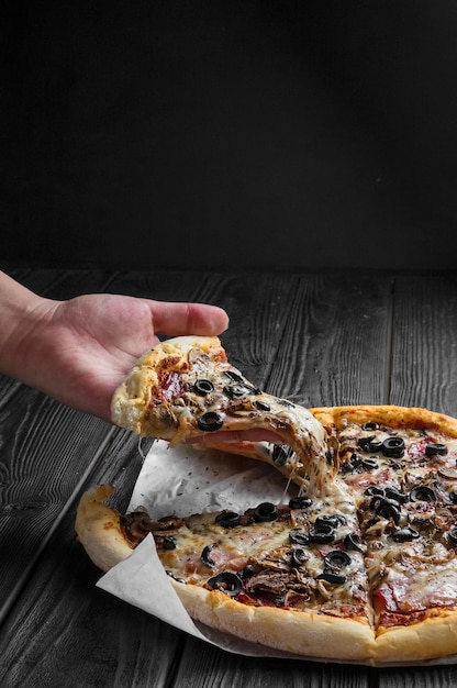 Traditional italian pizza on dark black wooden board, piece of pizza in hand,