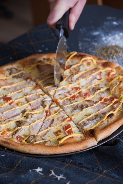 Traditional Italian pizza with chiken on dark blue stone table. Man cuts pizza with a knife