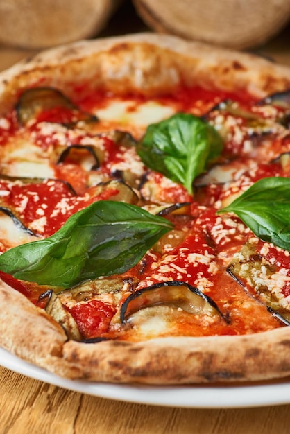 Traditional Italian pizza with eggplants mozzarella basil and tomatoes on wooden background