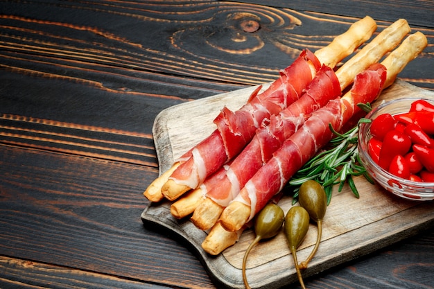 Traditional italian snack prosciutto crudo bread sticks, peppers and capers