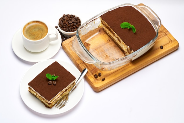 Traditional italian tiramisu dessert in glass baking dish portion on plate and cup of coffee isolated on white