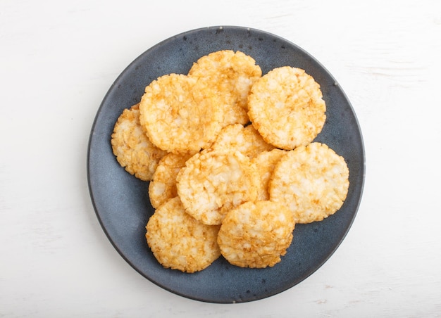 Traditional japanese rice chips cookies with honey and soy sauce on a blue ceramic plate on a white wooden background. Top view, flat lay, close up.